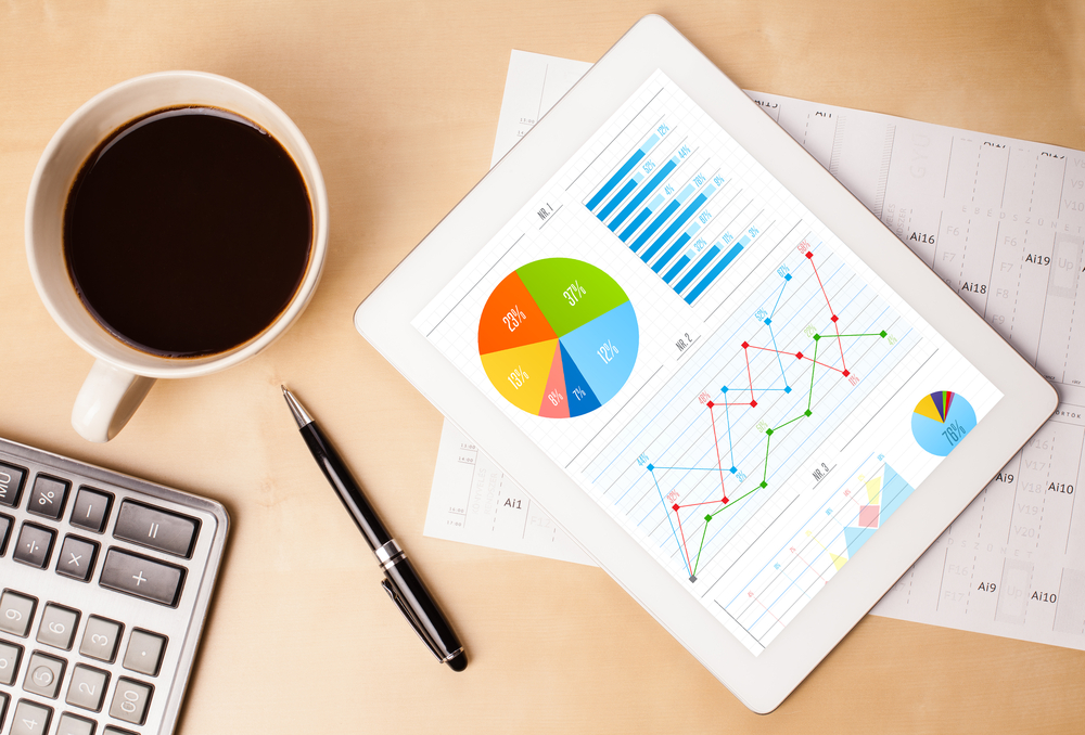 Workplace with tablet pc showing charts and a cup of coffee on a wooden work table close-up Workplace with tablet pc showing charts and a cup of coffee on a wooden work table close-up